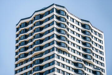 Fototapeta premium Contemporary multi story apartment building with curved balconies and geometric facade against clear blue sky, representing new housing development and modern city living.