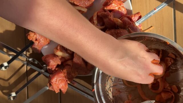 A person's hands are visible holding and placing cooked meat pieces into a metal basin set on a wooden surface, the basin already contains cooked pork ribs and other pieces of food