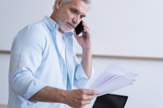 Busy mature business man talking on mobile phone in office