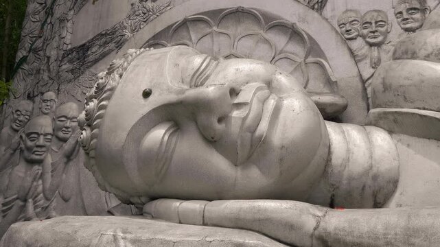 A close-up of Reclining Buddha stone statue with bas-relief depicting praying monks &ndash; the students of the Buddha. Long Son Pagoda in Nha Trang, Vietnam. Shot in motion
