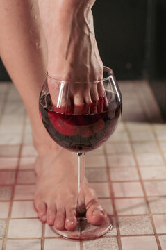 Foot fetish. A woman dips her toes in a glass of red wine.