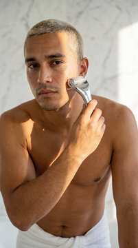Young man using metal facial roller on cheek for morning skincare routine