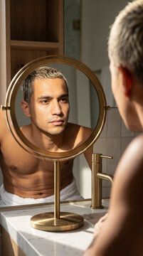 Contemplative young man looking at his reflection in round vanity mirror