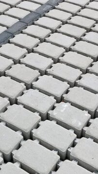 Parking renovation. light grey interlocking pavers staged on gravel in straight repeating rows, with visible seams and joints, rough cement textures, scattered debris, daylight.