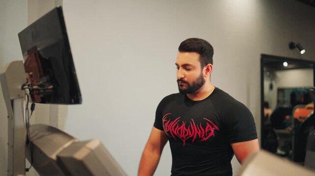 Focused bearded male athlete in a black graphic compression shirt doing treadmill walking exercise for stamina building and physical conditioning.