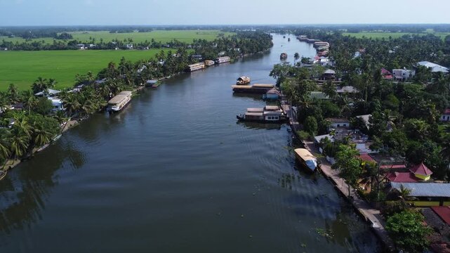 High Angle Aerial View of Kerala Backwater Canal with Traditional Houseboats Moored Along Shore. Drone Footage of Serpentine Backwater Canal and Waterfront Homes in Rural Kerala Village.
