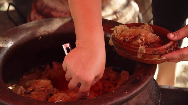 Cook serves traditional cabbage from a large pot into a clay bowl at a Serbian food festival. Close-up shows rustic Balkan cuisine and local culinary culture