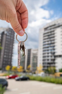 Hand Holding House Keys with Metal House Keychain against Modern Residential Complex Vertical