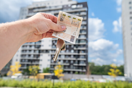 Close up of Hand Holding Keys and Polish Zloty Money Bills in Front of Residential Complex