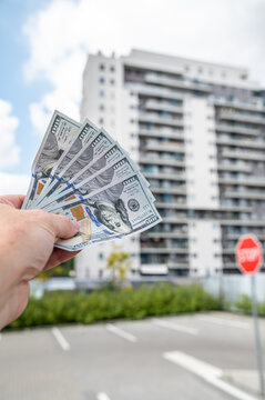 Male Hand Holding US Dollar Money Bills in Front of Modern Residential Apartment Building Vertical