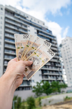 Vertical View of Hand Holding 200 Polish Zloty Banknotes Against Modern Apartment Skyscraper