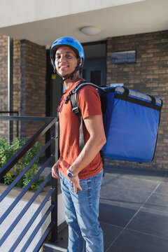 Delivery man with helmet and backpack stands outside of building entrance in the city