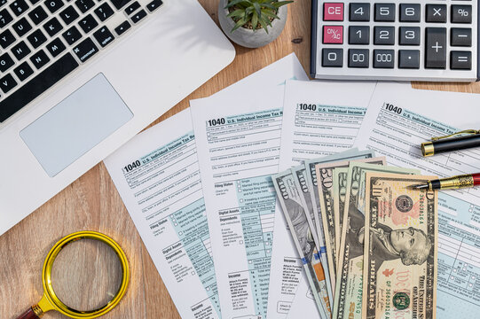 Magnifying Glass over US Dollar Bills and IRS Tax Form 1040 on Wooden Table for Audit Concept
