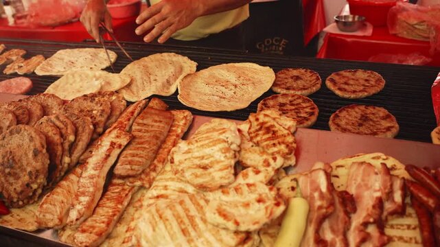 Vendor grills assorted meat and flatbread on a hot barbecue at a food stall. Close-up shows street food, outdoor cooking, and Serbian cuisine