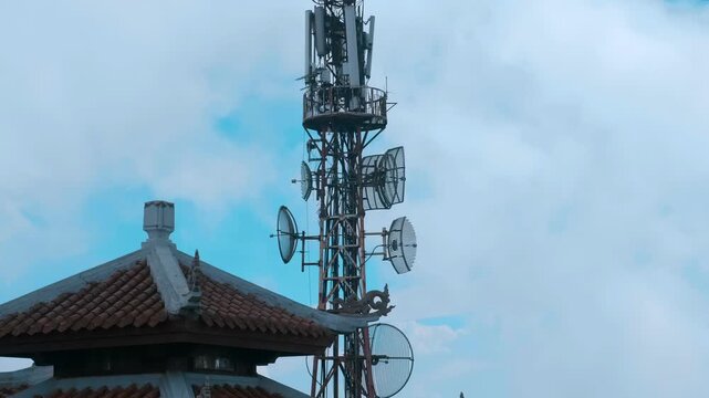 The silhouette of Buddhist Temple with traditional Asian style bended tiled roofs with a large telecommunications and broadcasting lattice tower with multiple antennas that sits on the mountain peak i