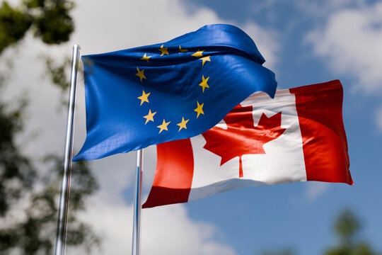 Flags of the European Union and Canada waving in the wind against a blue sky, symbolizing international relations, diplomatic alliance, economic partnership, trade agreements, and cooperation.