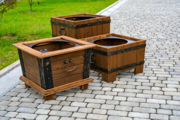 Empty decorative flower stands shaped as chests with wrought iron handles on paved walkway, urban landscaping concept © Dmitrii Labrador