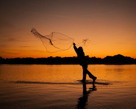 Silhouette of a traditional fisherman throwing a cast net into the water at golden sunset, coastal lifestyle and active fishing motion concept
