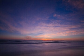 Obraz premium Tranquil ocean sunset with silky water ripples under a dramatic purple and pink twilight sky scenic beach landscape 