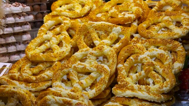 Customer choosing a cheesy pretzel at a market stall. Golden baked pretzels covered in cheese displayed at a festive market stall, where a person's hand reaches out to select of the savory pastry