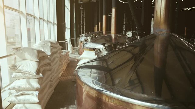 Industrial beer manufacturing facility with brewery tanks, brewing equipment and ingredient sacks for beverage production.