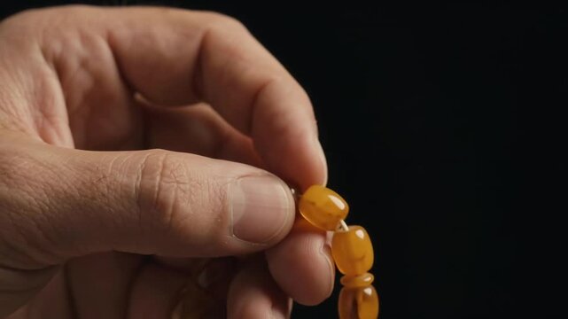 Close Up Of Muslim Man Hand Counting Amber Tasbih Beads In Prayer Over Black Background For Islamic Ramadan Meditation And Dhikr