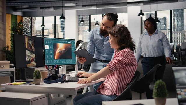 Two colleagues wait for AI text-to-video generation on a computer showing futuristic Mars and outer space visuals, using artificial intelligence to create cosmic universe materials.