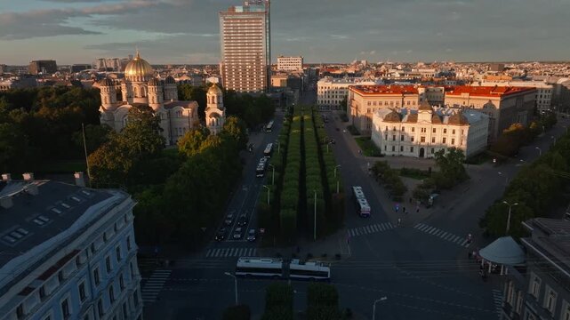 Riga boulevard tree alley, cathedral and hotel tower at sunset from drone. Aerial shot gliding along the avenue in Riga, Latvia, with tree alley, buses and cars, golden domed orthodox cathedral.