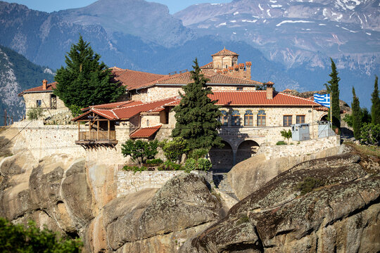 Holy Trinity Monastery perched on a rocky outcrop in the Meteora landscape of Greece, surrounded by dramatic rock formations and mountains.
