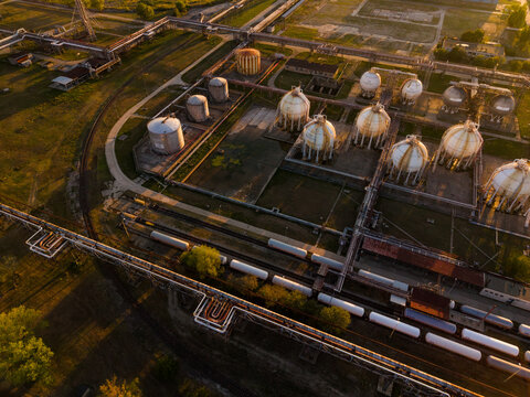 Spherical storage tanks beside rail tank wagons seen from above. White vessels stand on concrete pads above parallel tracks, with pipes crossing the lower foreground.