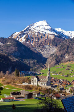 Lungern village surrounded by the Swiss Alps, with snow-covered mountain peaks rising behind the settlement. The scenic landscape is located in Obwalden canton, Switzerland.