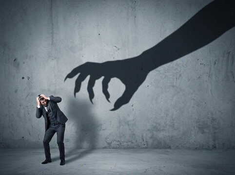Frightened business person reacting to a huge monster claw shadow looming on the background, representing fear, threat, workplace stress, business risk and uncertainty.