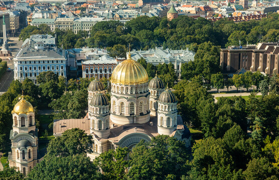 Nativity of Christ Cathedral among park trees in morning light from above, Riga, Latvia. Drone high viewpoint on the orthodox church with gilded domes and pale striped facade among green park trees.