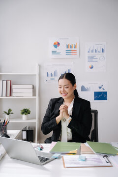 Excited Businesswoman Celebrating Success at Desk: A focused businesswoman in a professional suit beams with joy and claps her hands together in excitement while sitting at her desk.