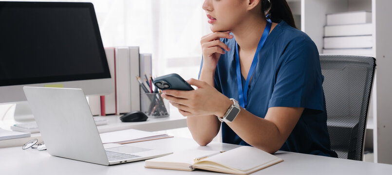 Young Professional Working in Office: A focused young woman sits at her desk in a modern office, engrossed in her work on a laptop and smartphone, with a notebook open for jotting down ideas.