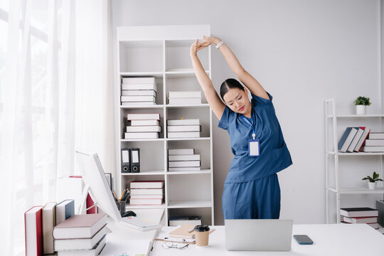 Nurse stretching at desk: A nurse in blue scrubs performs a side stretch at her desk, maintaining flexibility and well-being during a demanding shift.