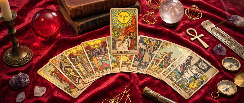 Fortune teller and whitcraft concept with tarot cards spread on red velvet surrounded by a magic crystal ball, gold bracelet, a book and a wooden box