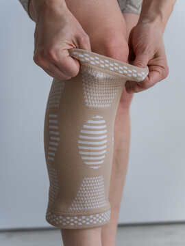 A Caucasian woman suffers from knee pain and wears a supportive elastic knee brace.