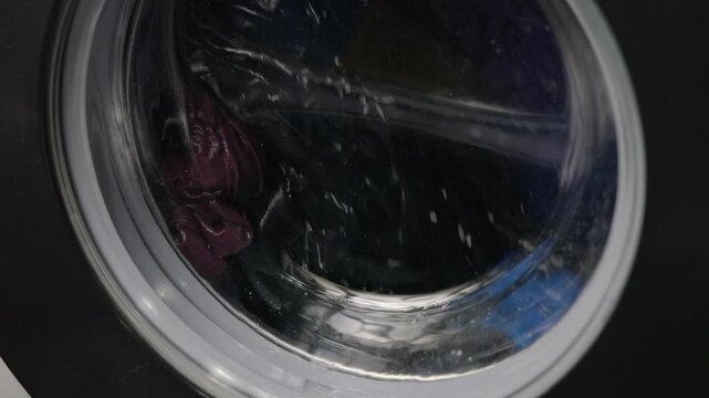Close-up of clothes spinning inside washing machine drum. Colorful laundry tumbling inside a modern washing machine during a spin cycle, with soapy water splashing against the glass door