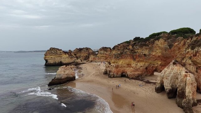 People enjoying sandy beach with rock formations in alvor, portugal