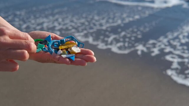 Person holding microplastics collected from the ocean beach. Woman's hands holding a handful of small plastic particles and microplastics collected on a sandy beach, highlighting the growing problem