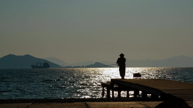 Resting man with fishing rod against morning. A view of resting boy silhouette admire the sunrise time during fishing