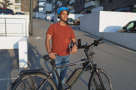 young man stands next to his electric bicycle on a street in a city