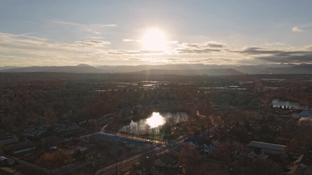 Aerial view showing a vast cityscape with a lake, mountains, and the sun setting 4K Arvada Colorado