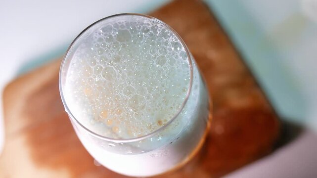 Top view (close-up) of a glass of beer on a wooden board. Bubbles burst in the dense foam of the beer. A glass of draft beer on the table. A bar table. POV: drinking beer; having a beer. A restaurant 