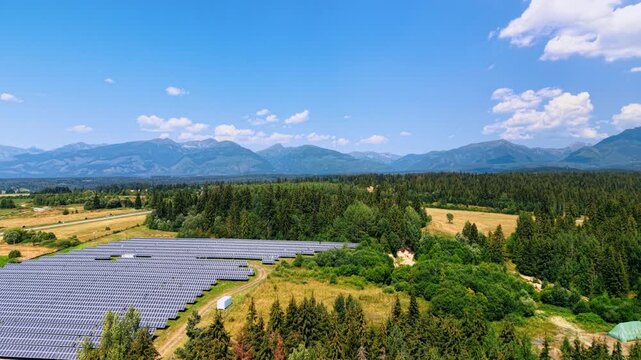 Solar panel field below wooded foothills of the Tatra Mountains. Photovoltaic rows enter from the lower left beside shrubs, with a broad sky above distant peaks.