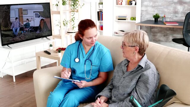 nurse writes consultation details on a clipboard beside an older woman, highlighting care documentation, communication and attentive senior healthcare, with additional focus on clinical notes.