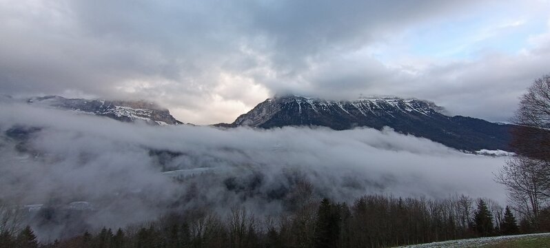 un impressionnant paysage de montagne envelopp&eacute; de brume, sous un ciel charg&eacute; de lourds nuages gris.