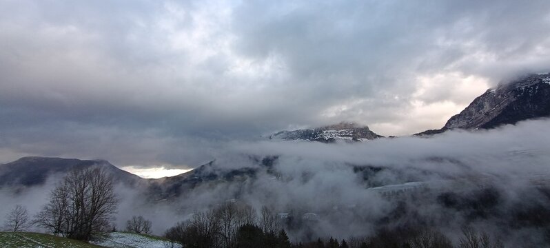 un impressionnant paysage de montagne envelopp&eacute; de brume, sous un ciel charg&eacute; de lourds nuages gris.