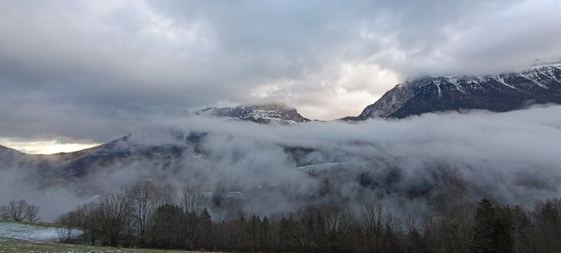 un impressionnant paysage de montagne envelopp&eacute; de brume, sous un ciel charg&eacute; de lourds nuages gris.